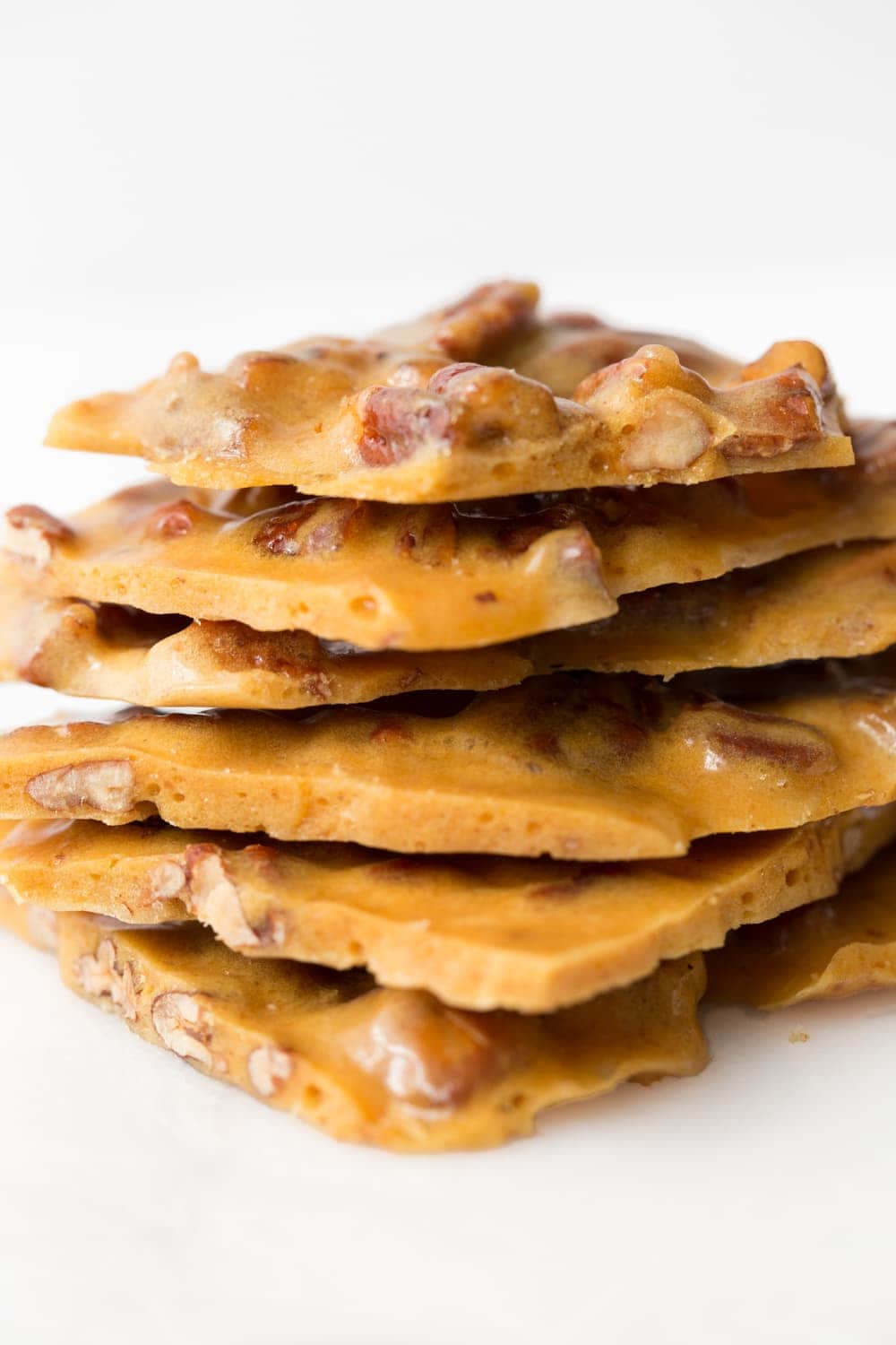 Vertical closeup photo of 15 Minute Microwave Pecan Brittle in a stack against a white background.