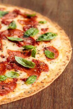 Close up vertical picture of easy thin crust pizza with basil and pepperoni