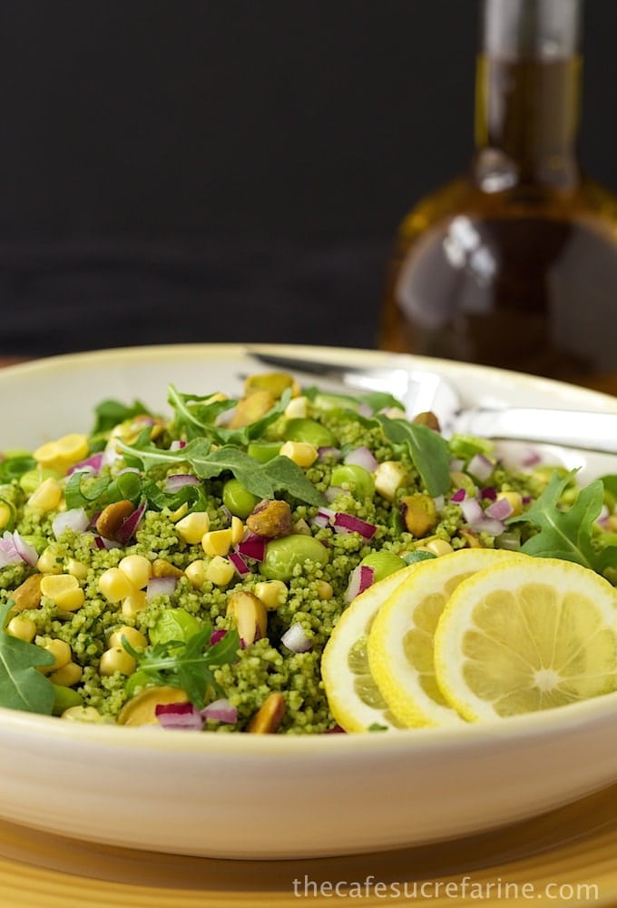 Photo of a bowl of Green on Green Couscous Salad on a yellow placemat and a bottle of EVOO in the background.