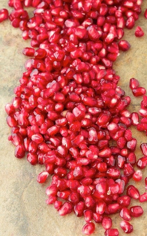 Vertical photo of pomegranate seeds (arils) on a slate surface.