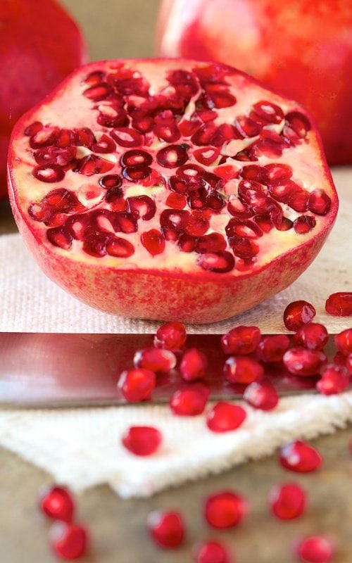 Vertical closeup photo of a sliced pomegranate and it's arils.