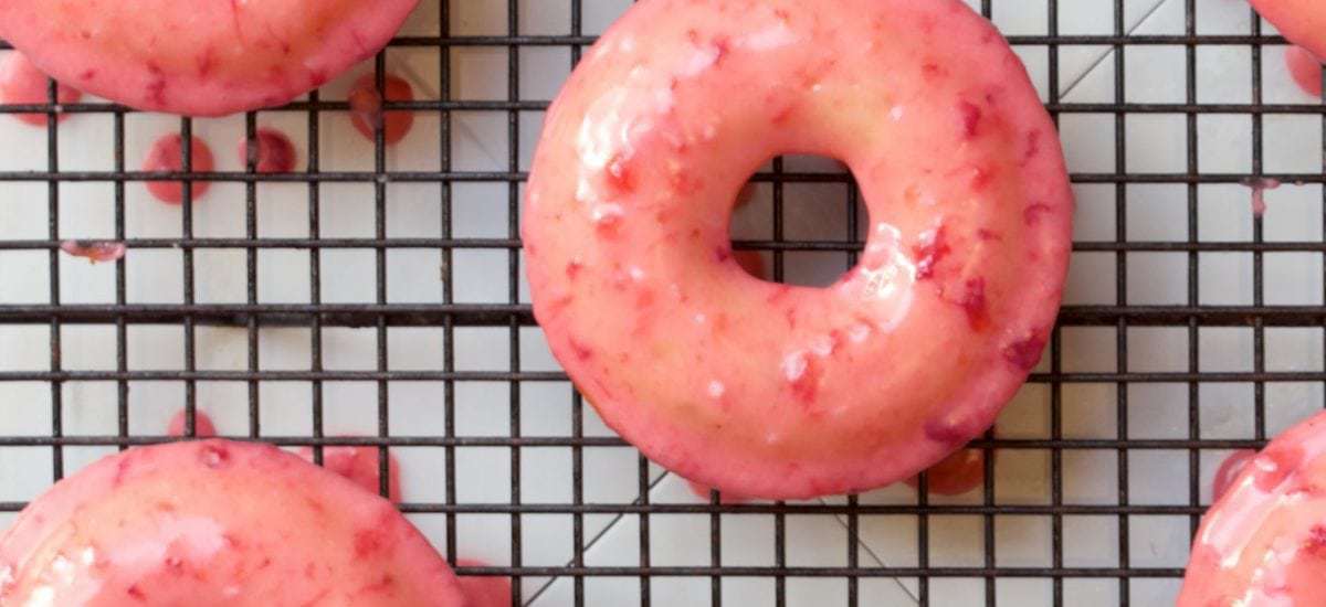 Overhead photo of Baked Buttermilk Donuts with Fresh Strawberry Glaze on a black cooling rack.