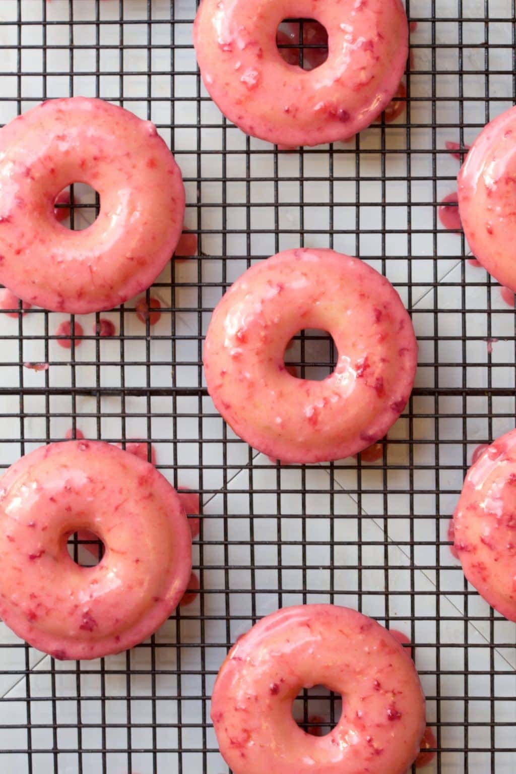 Overhead photo of Baked Buttermilk Donuts with Fresh Strawberry Glaze on a black cooling rack.