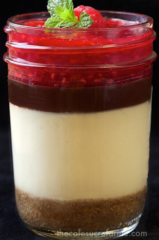 Layered Cheesecake Jars. Golden, buttery graham cracker crust covered with light creamy cheesecake, a layer of silky smooth ganache and fresh raspberry sauce. A heavenly combination!!