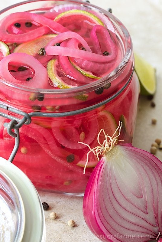 Photo of a glass jar of Pickled Red Onions with a sliced red onion leaning against it.