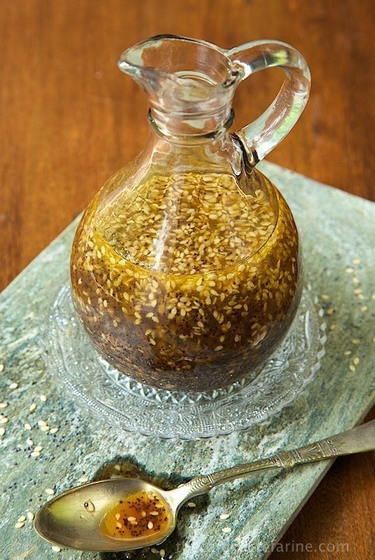 Vertical photo of Asian Honey-Sesame Salad Dressing in a glass cruet resting on a slate platter.