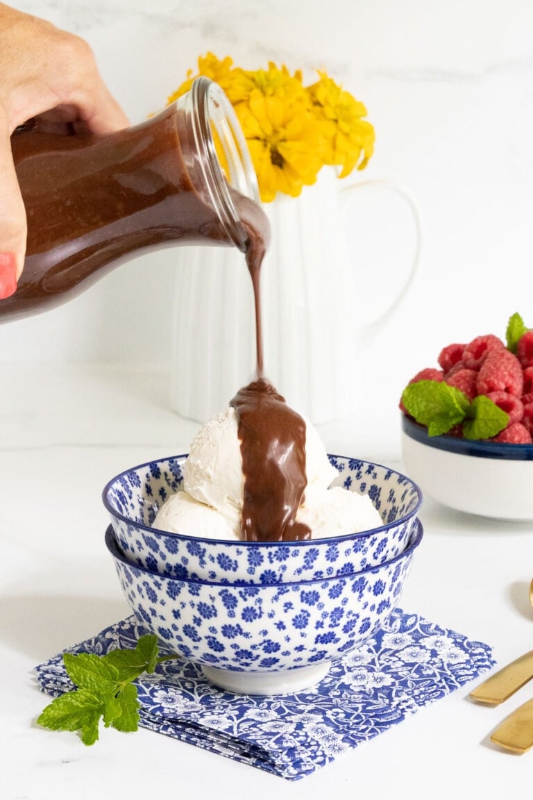 Vertical picture of Ridiculously Easy Hot Fudge Sauce poured over vanilla ice cream in a blue and white bowl.