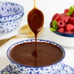 Horizontal photo of a bowl of Ridiculously Easy Hot Fudge Sauce with a spoon dripping the sauce back into a blue and white bowl.