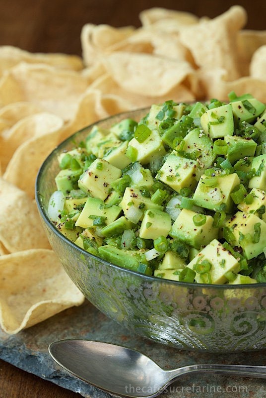 Closeup photo of a glass serving bowl filled with Best Avocado Salsa with tortilla chips in the background.