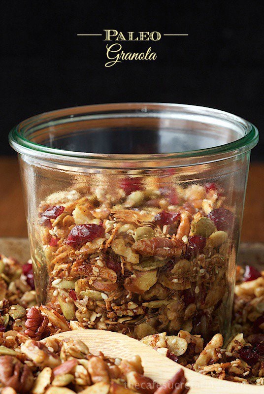 A Weck jar full of Paleo Granola surrounded by paleo Granola and a wooden spoon on a wood table.