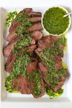 Vertical image of Grilled Tri-Tip with Chimichurri Sauce on a white rectangular platter.
