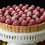 Vertical picture of French Chocolate Tart with Brown Butter Crust topped with fresh raspberries on a white cake stand