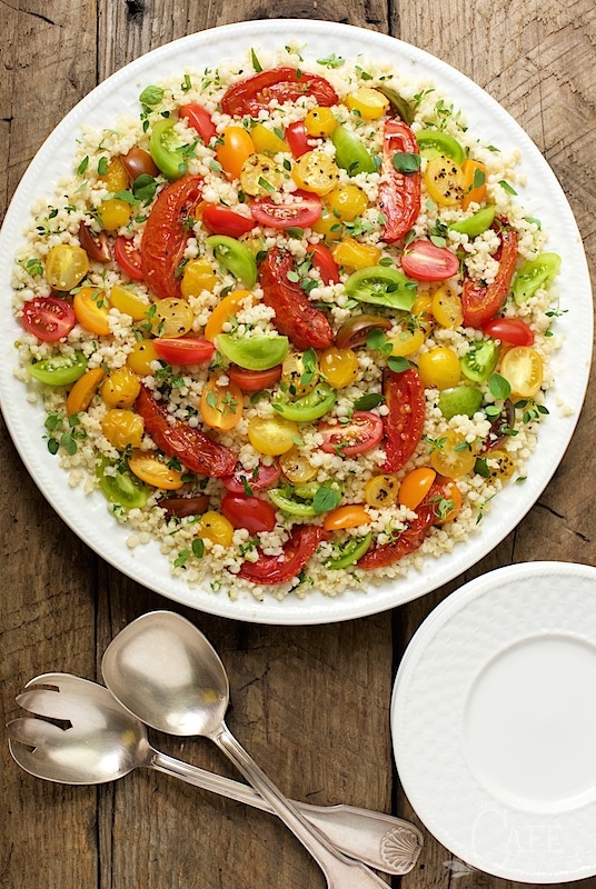 Photo of a Tomato Party Couscous Salad on a white serving plate on a barnboard table surface.