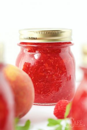 Glass jar of peach raspberry freezer jam with a gold lid, surrounded by fresh raspberries and peaches.