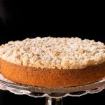 Horizontal closeup photo of a person holding a Easy Overnight Coffee Cake on a glass serving plate.