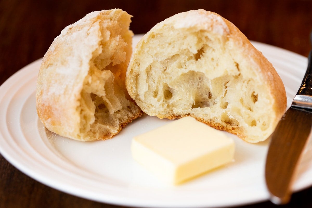 Extreme horizontal closeup photo of a Ridiculously Easy Artisan Roll open with a pat of butter on the plate.