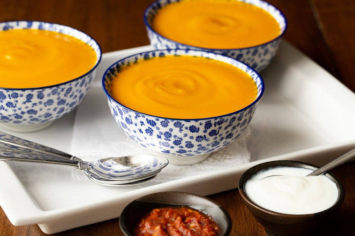 Horizontal closeup photo of Roasted Thai Carrot and Sweet Potato Soup in blue and white patterned soup bowls.