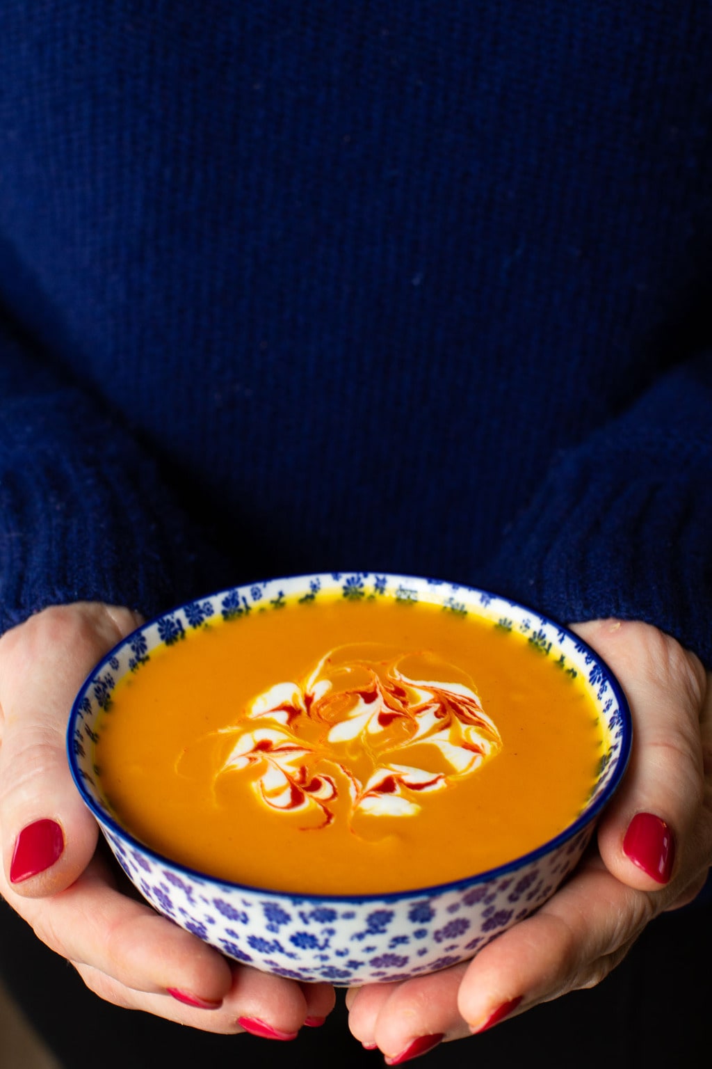 Vertical extreme closeup photo of a person holding a bowl of Roasted Thai Carrot and Sweet Potato Soup.