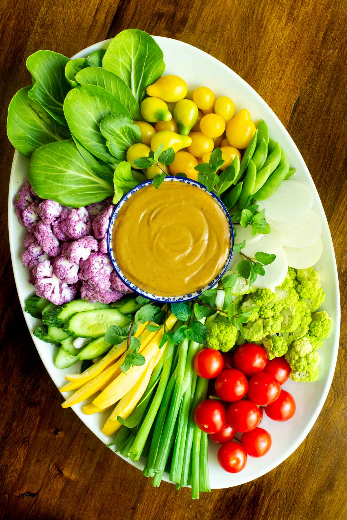 Overhead vertical photo of an oval appetizer platter featuring fresh veggies and 5 Minute Easy Peanut Sauce.