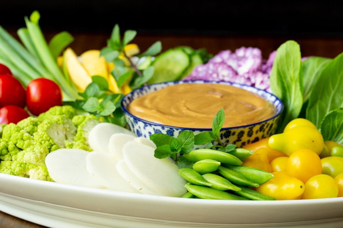 Horizontal closeup photo of an appetizer plate filled with fresh vegetables and featuring 5-Minute Easy Peanut Sauce.