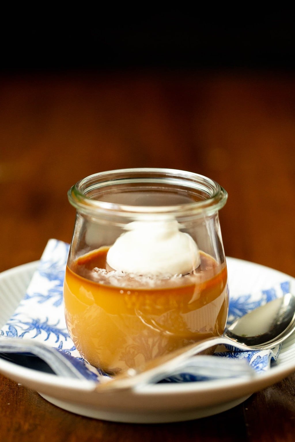 Vertical closeup photo of Butterscotch Pots de Crème in a glass Weck jar on a blue and white patterned napkin.