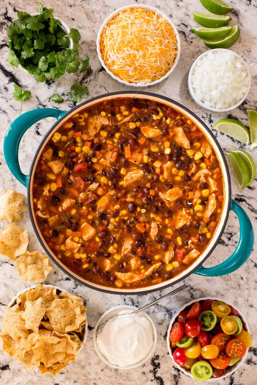 Overhead vertical photo of Chicken Black Bean Chili in a turquoise dutch oven with small bowls of toppings and garnishes.