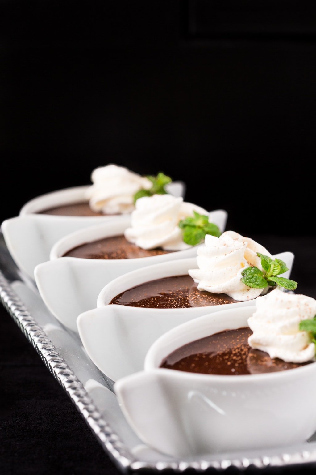 Vertical closeup photo of Chocolate Pots de Creme in white ramekins with mint and whipped cream.