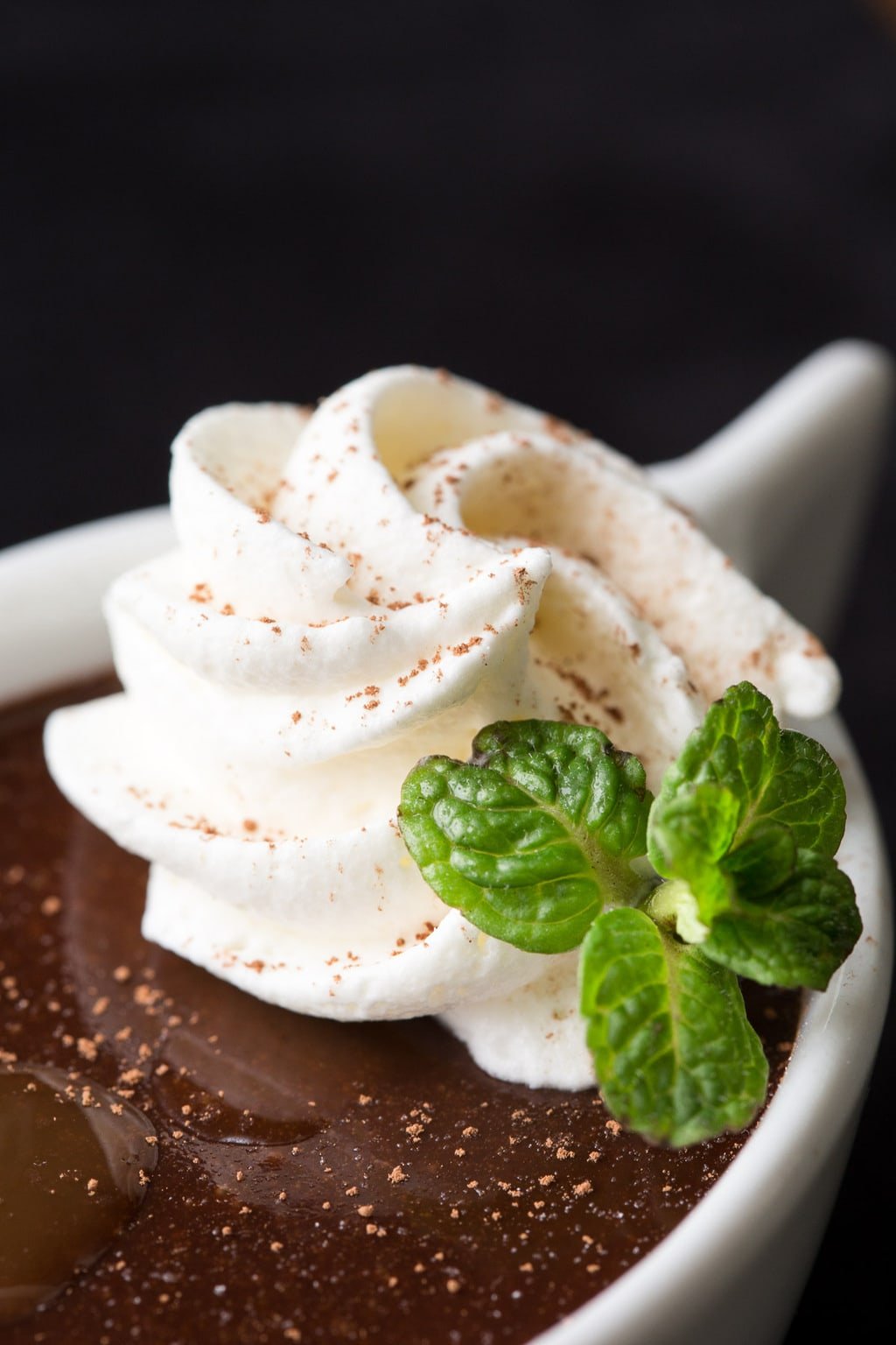 Vertical extreme closeup photo of a Ridiculously Easy Blender Chocolate Pots de Crème garnished with whipped cream and fresh mint leaves.