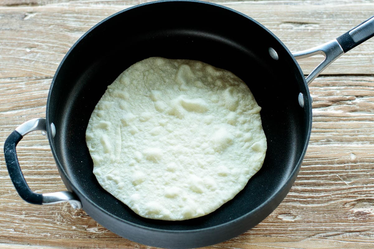 Homemade flour tortilla puffing up in a hot skillet as it cooks, showing bubbles forming on the surface—a key step in making soft tortillas from scratch.