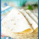 A vertical graphic showing a stack of homemade flour tortillas with overlay text that reads “Homemade Flour Tortillas - So Easy, So Delicious!!” on a colorful towel background, styled for Pinterest.