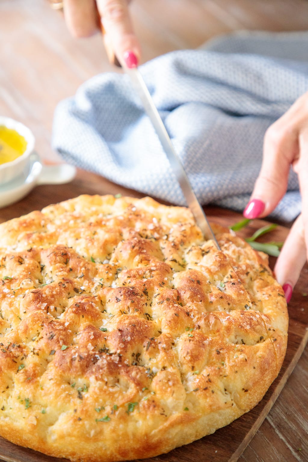 Vertical closeup photo of a person slicing a piece of Ridiculously Easy Focaccia Bread on a wood table.