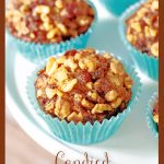 Vertical closeup photo of a batch of Candied Walnut Date Banana Muffins in turquoise cupcake liners on a white pedestal serving plate with a text graphic title on the bottom.