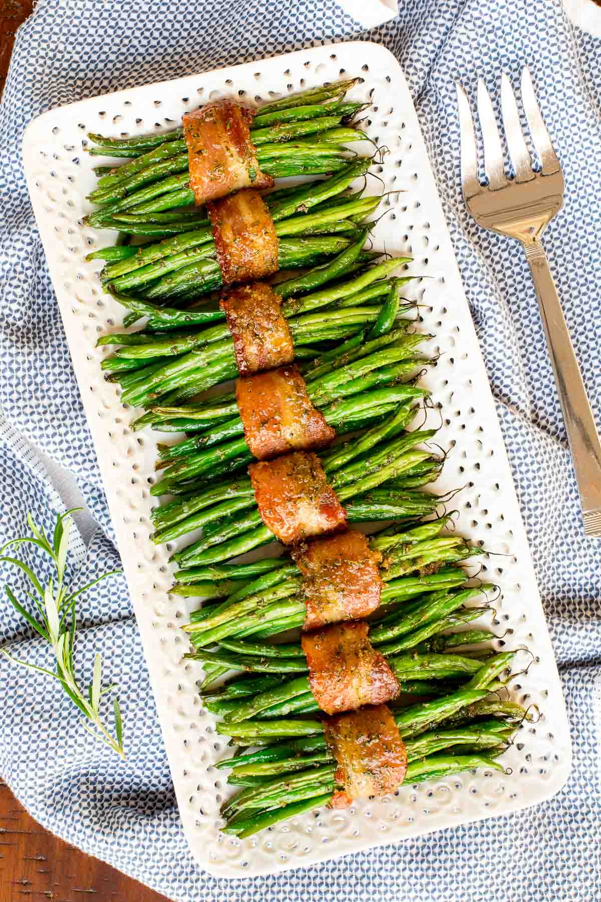 Vertical overhead photo of Make-Ahead Bacon Wrapped Green Beans wrapped in bundles on a white lattice serving platter.