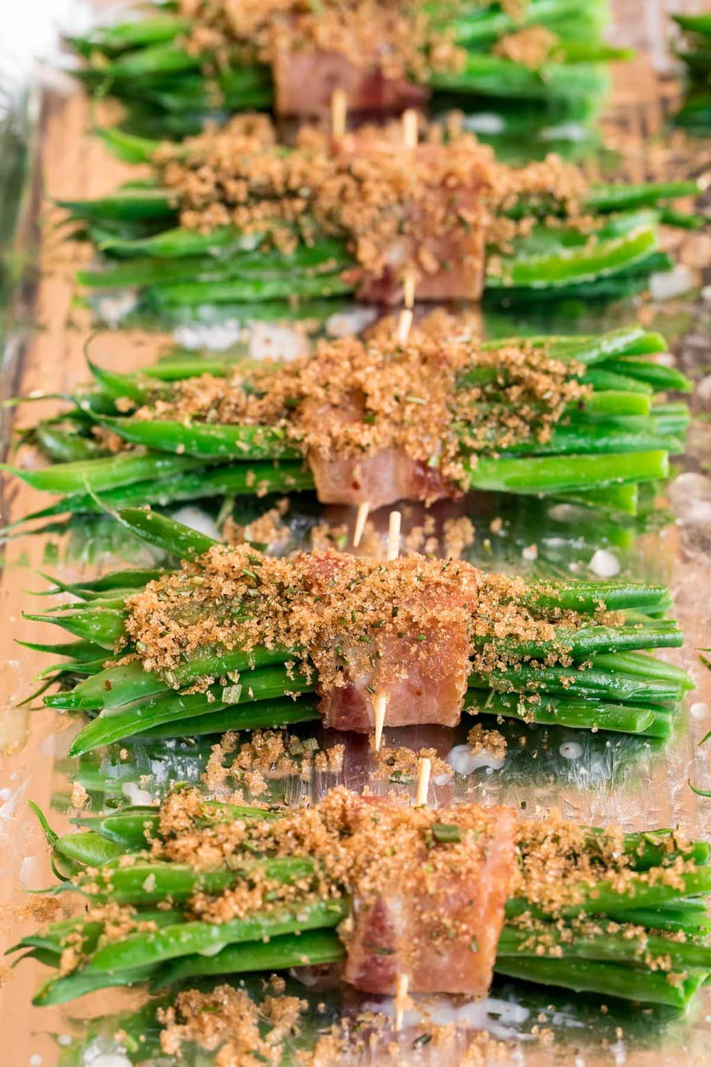 Vertical process photo of Make-Ahead Bacon Wrapped Green Beans being prepared for the oven.