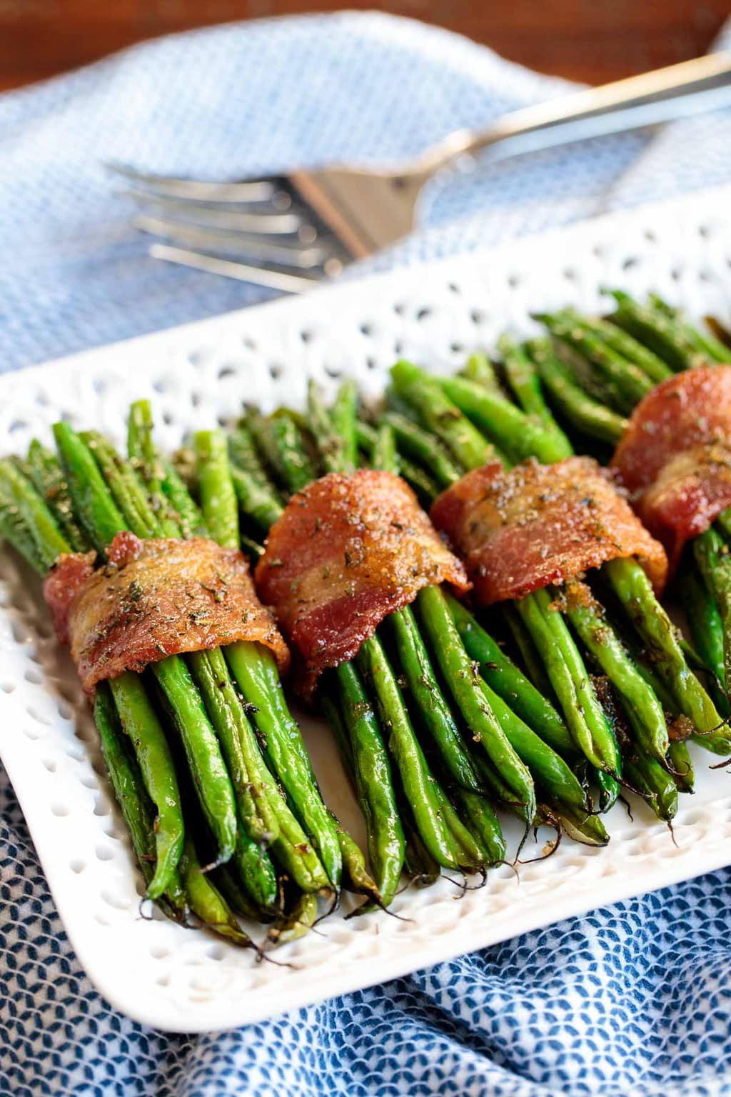 Vertical photo of bundles of Make-Ahead Bacon Wrapped Green Beans on a white lattice serving plate.