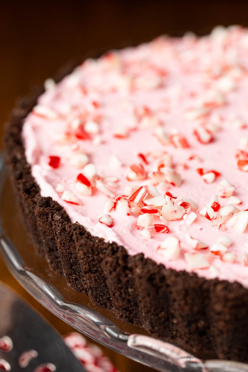 Vertical extreme closeup photo of the side and top of a Peppermint Candy Cane Tart on a glass serving plate.