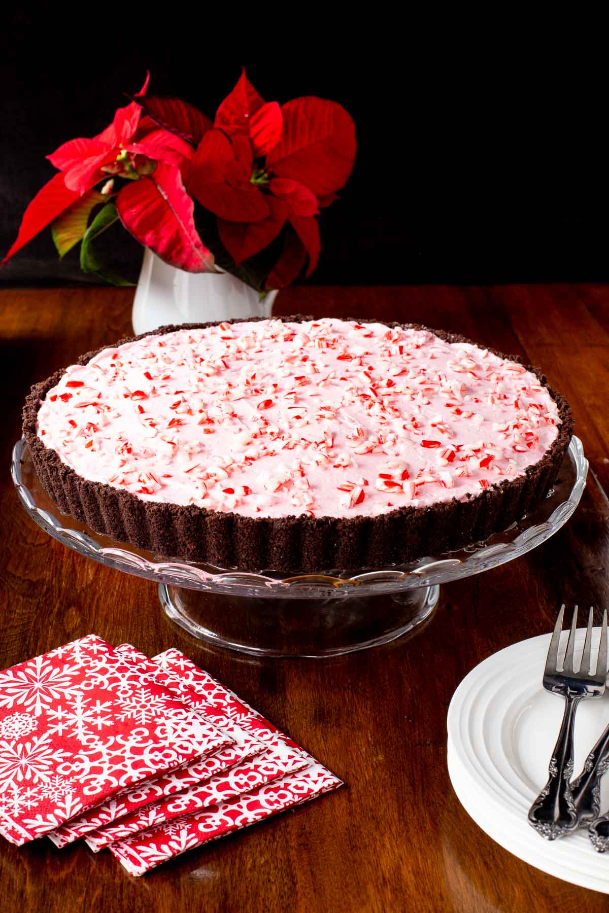 Vertical photo of a Peppermint Candy Cane Tart on a glass pedestal serving plate on a wood table.