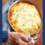 Vertical photo of a person holding a stainless steel baking pan full of Make Ahead Homemade Manicotti.
