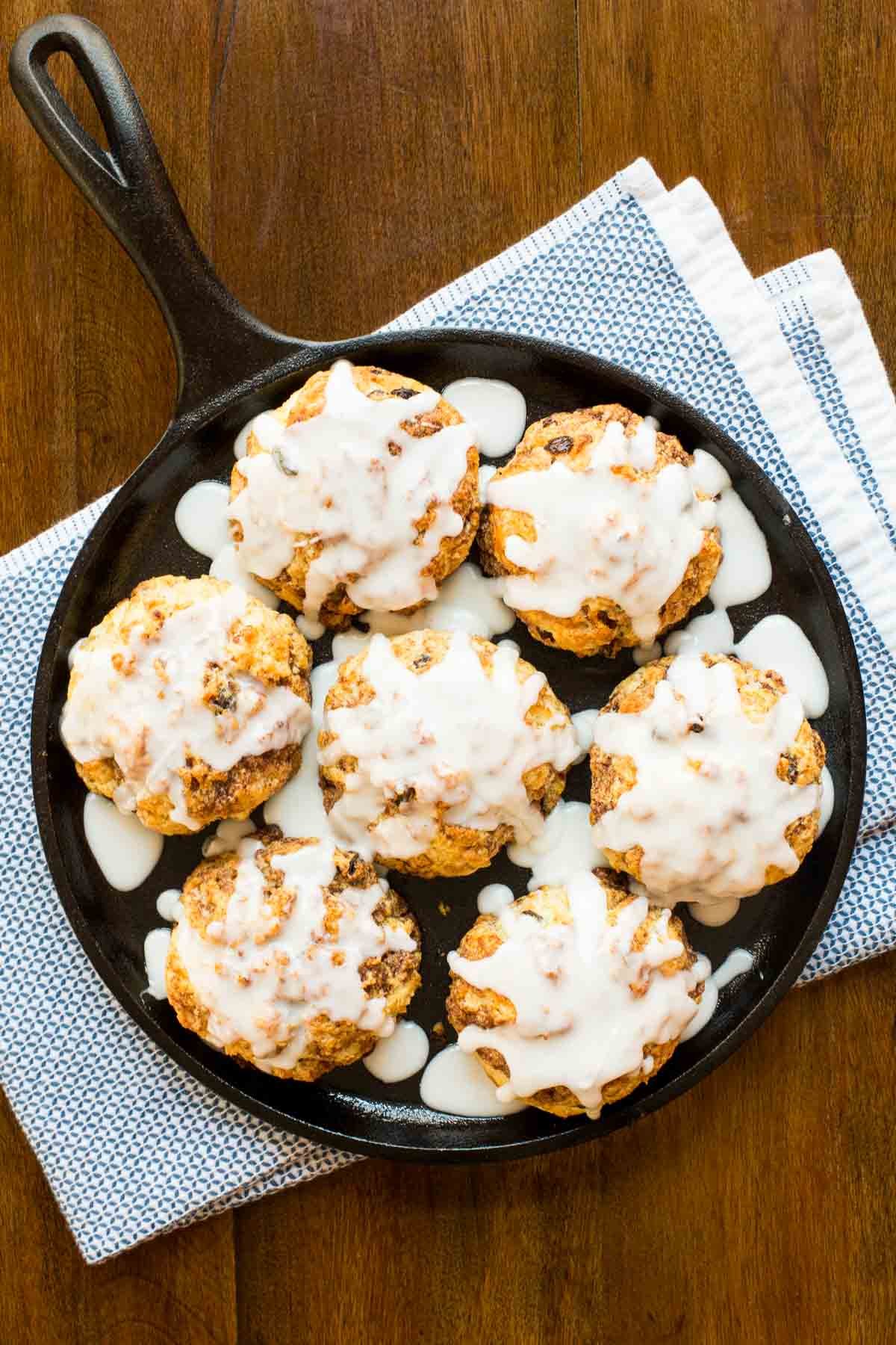 Vertical overhead photo of a cast iron skillet filled with Ridiculously Easy Cinnamon Raisin Biscuits on a wood table.