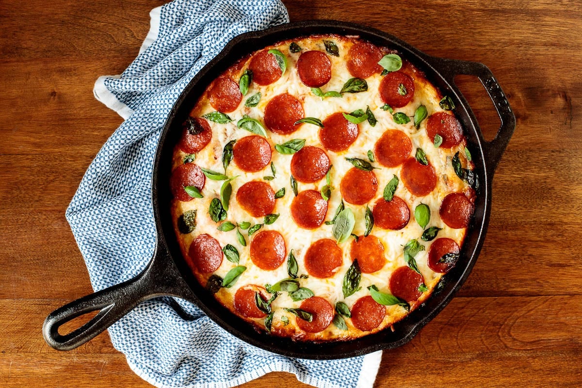 Horizontal overhead photo of a cast iron pan with a Pepperoni and Basil Pizza utilizing Easy Deep Dish Pizza Dough.