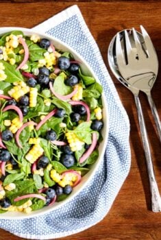 Horizontal overhead photo of a white serving bowl of Blueberry and Fresh Corn Spinach Salad on a wood table.