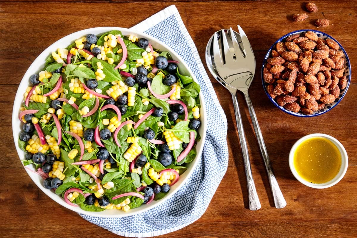 Horizontal overhead photo of a white serving bowl of Blueberry and Fresh Corn Spinach Salad on a wood table.