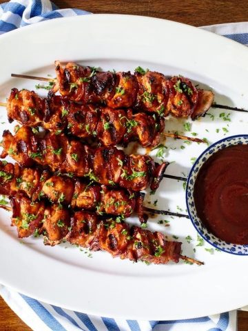 Horizontal overhead photo of Bacon Bourbon Barbecued Chicken Skewers on a white oval serving platter.