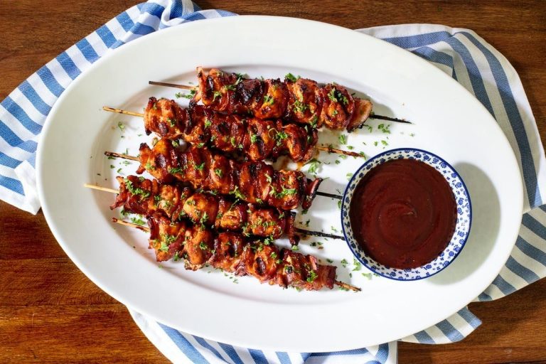 Horizontal overhead photo of Bacon Bourbon Barbecued Chicken Skewers on a white oval serving platter.