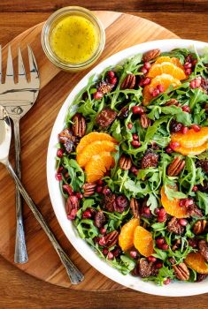 Horizontal overhead photo of a Cranberry Clementine Arugula Salad in a white marble serving bowl on a wood table.