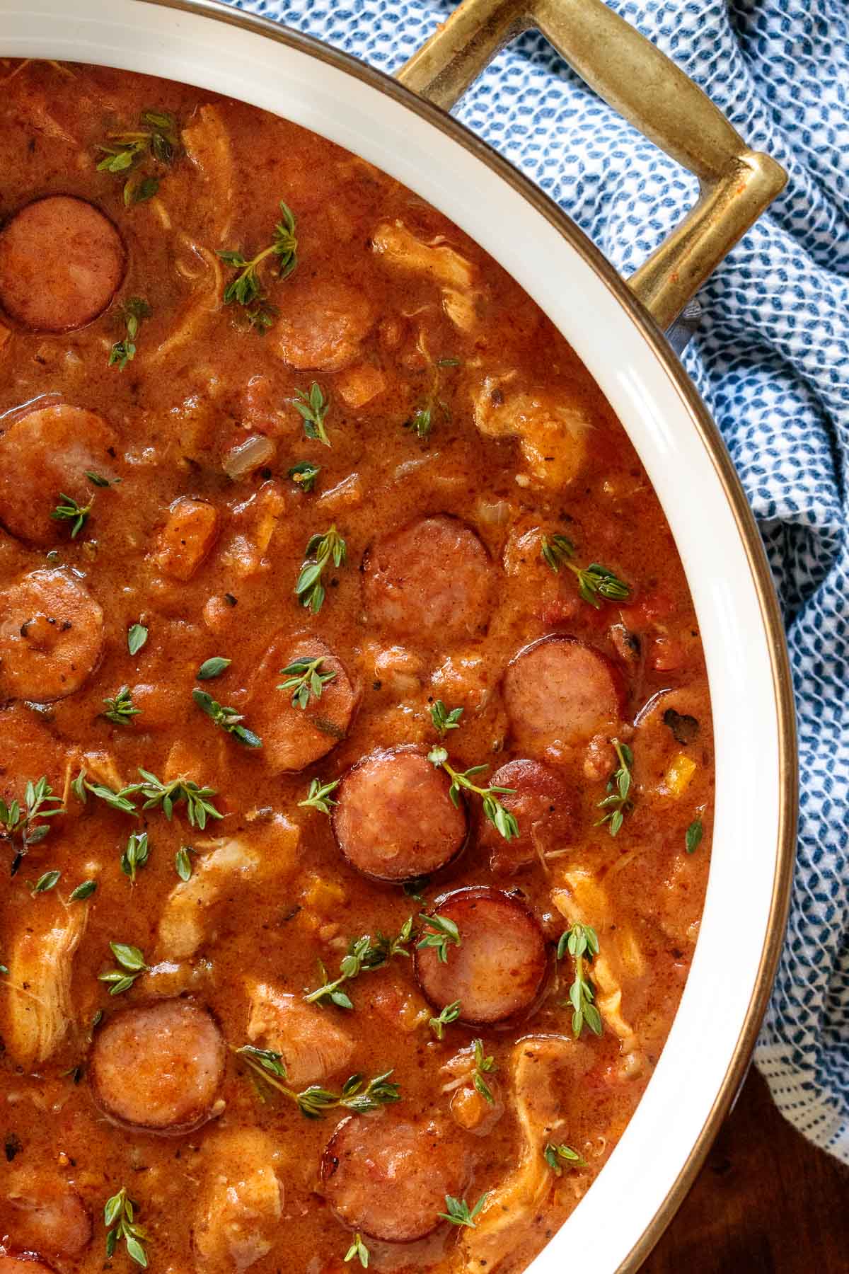 Vertical overhead closeup photo of a pot of Make-Ahead Chicken Andouille Gumbo next to a blue and white patterned cloth.