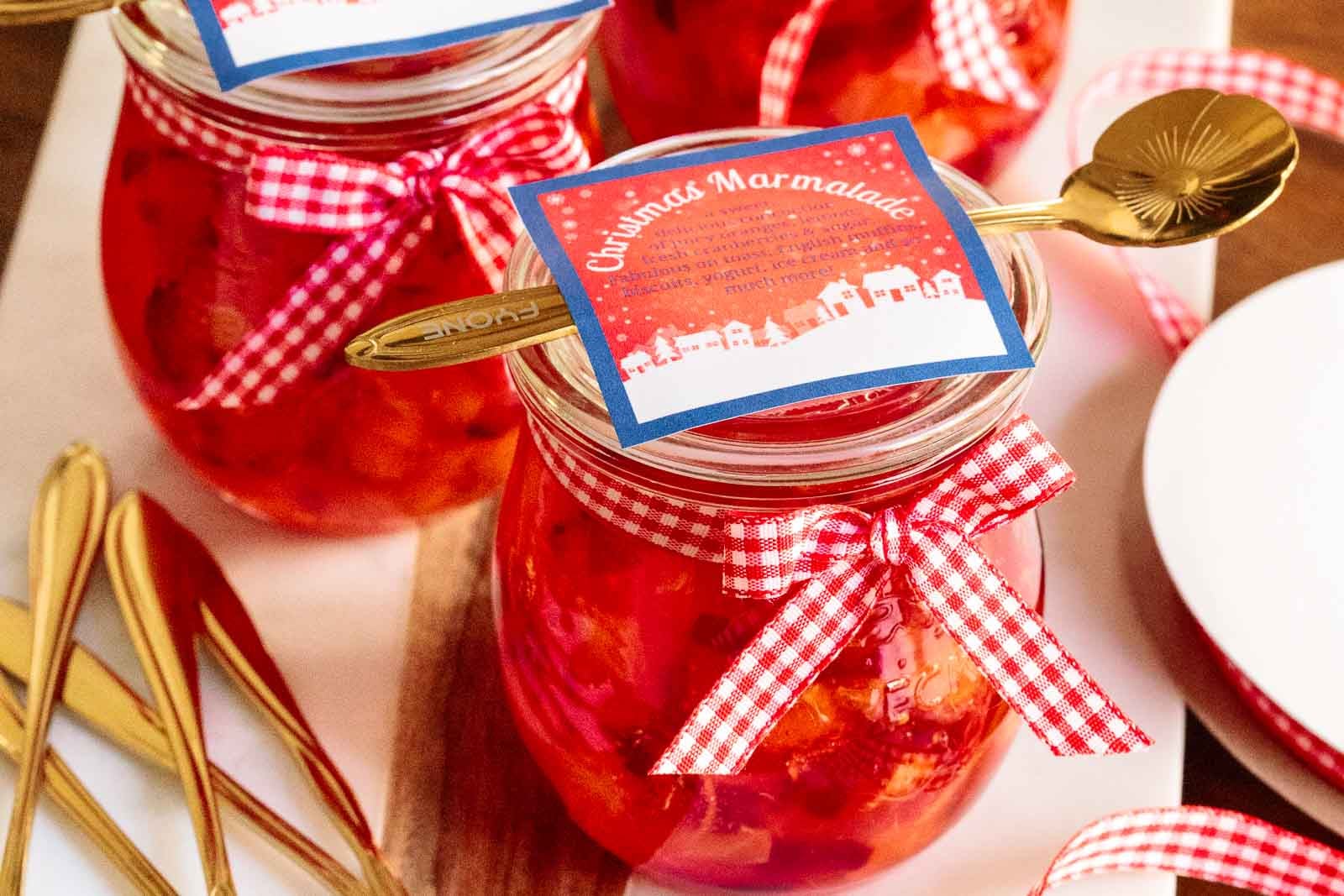 Jars of Orange Cranberry Christmas Marmalade with a label and decorative spoon on the top of each one.