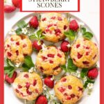 Vertical overhead photo of a batch of Ridiculously Easy Fresh Strawberry Scones surrounded by strawberry leaves, strawberries and strawberry flowers.