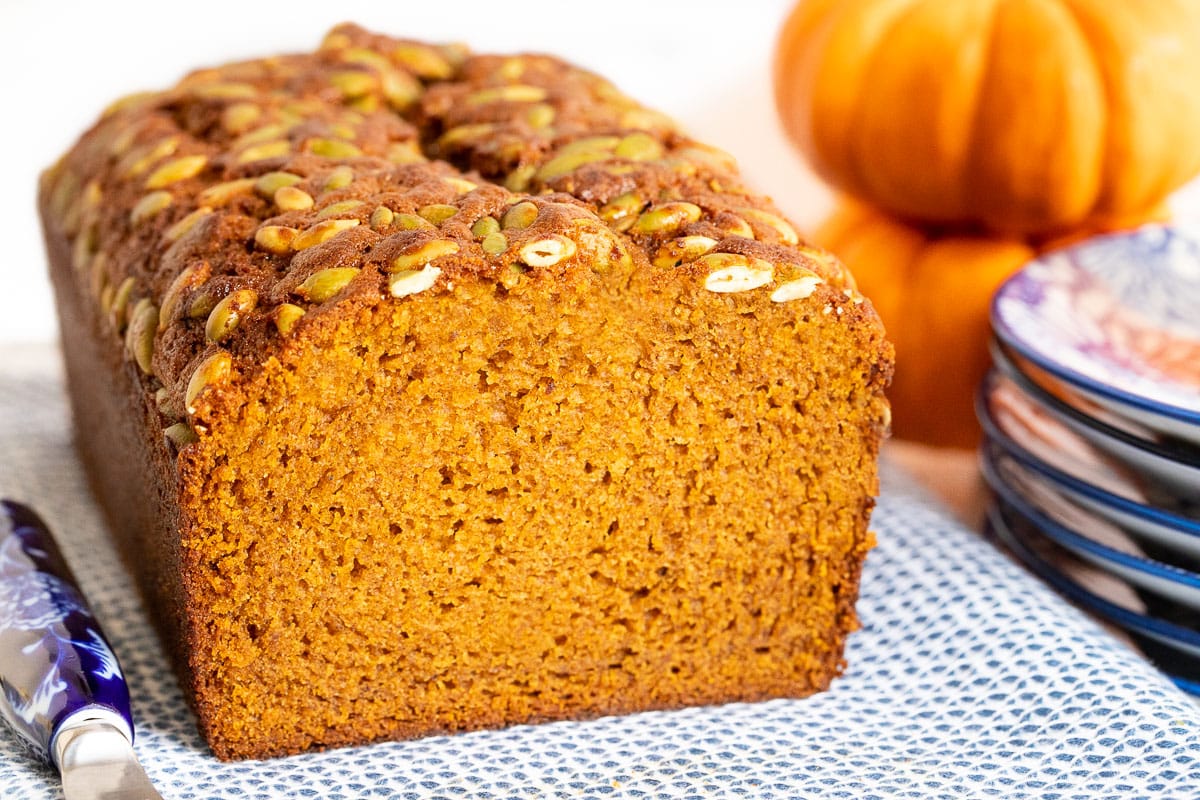 Horizontal closeup photo of a loaf of Better Than Starbucks Pumpkin Bread with mini pumpkins in the background.
