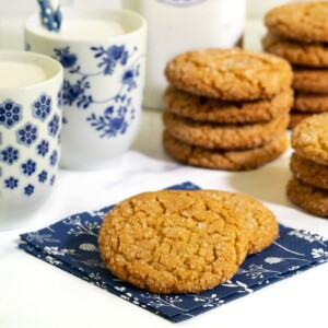 Horizontal photo of a batch of Crinkly Crackly Peanut Butter Cookies with glasses of milk in the background.